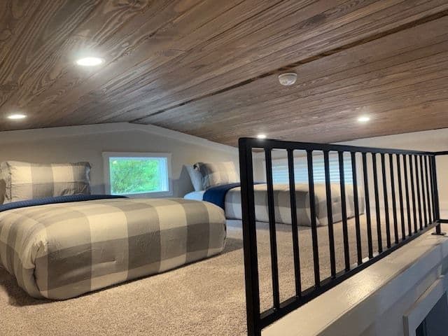 Loft under a wood-plank ceiling with a plaid bed and black stair rail