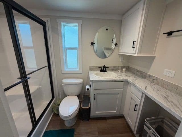 Bathroom with sliding glass shower, round mirror, white vanity and window