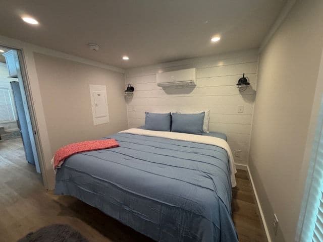 Bedroom, queen bed with blue spread and red throw, wall AC, soft gray walls