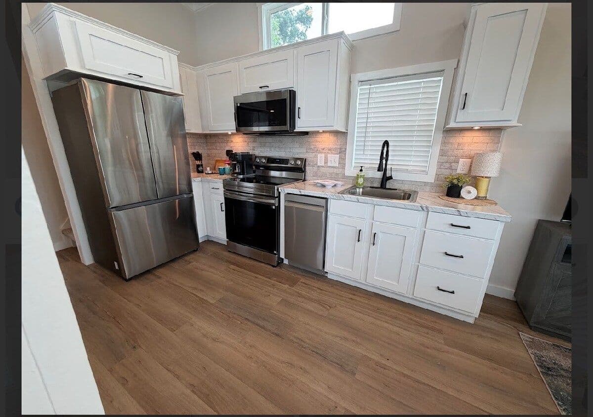 Kitchen with stainless fridge and range, white cabinets, window over the sink