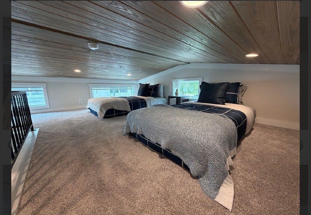 Loft with two beds in gray bedding under a plank ceiling