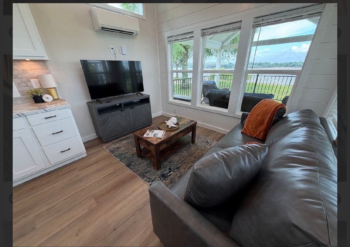 Living room with TV console and black leather sofa with orange pillow