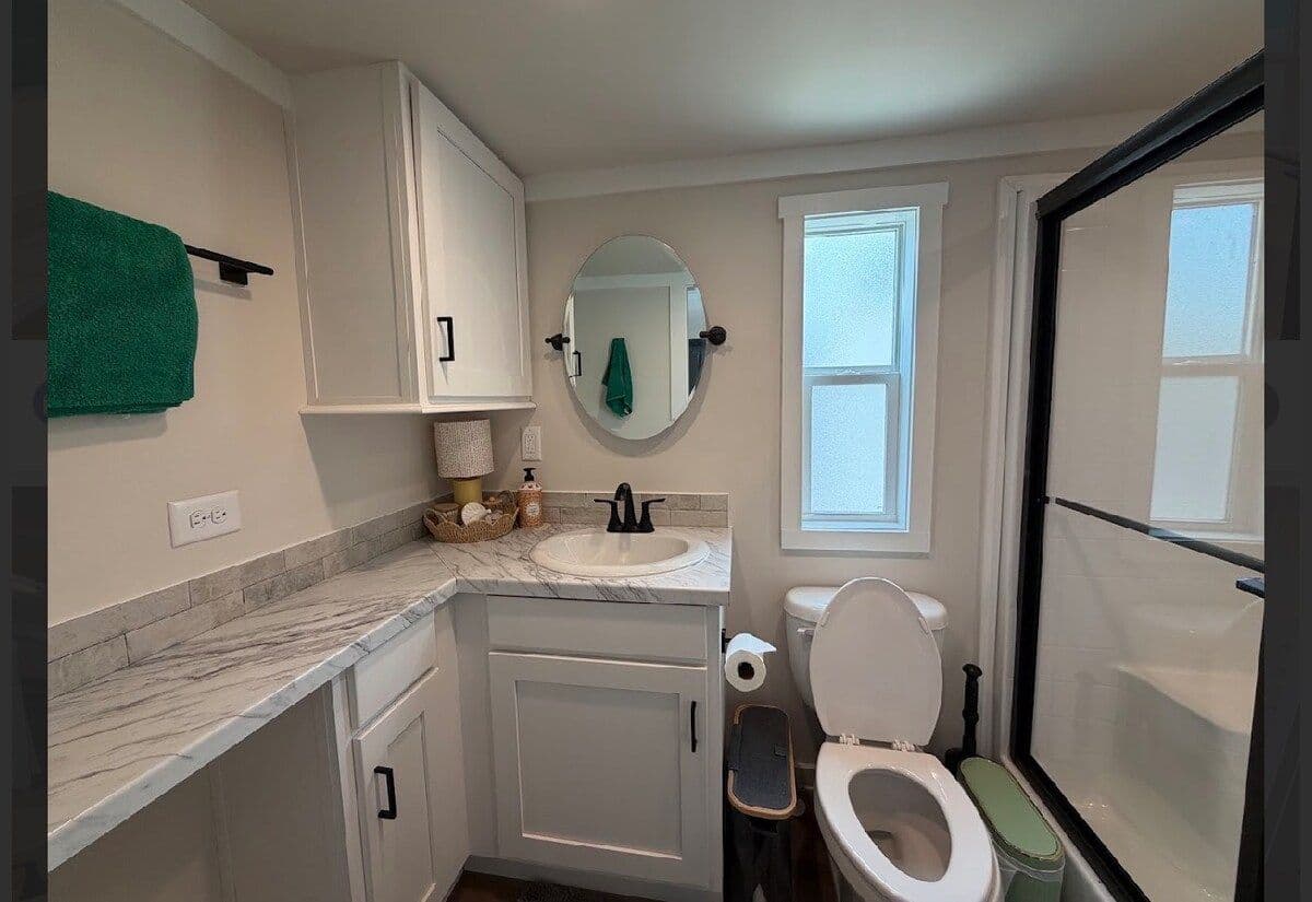 Bathroom vanity with green towel, round mirror, toilet and shower