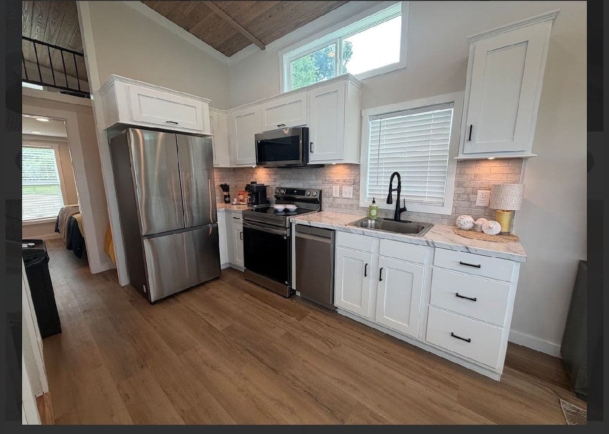 Kitchen with stainless fridge and range, white cabinets, stair rail above