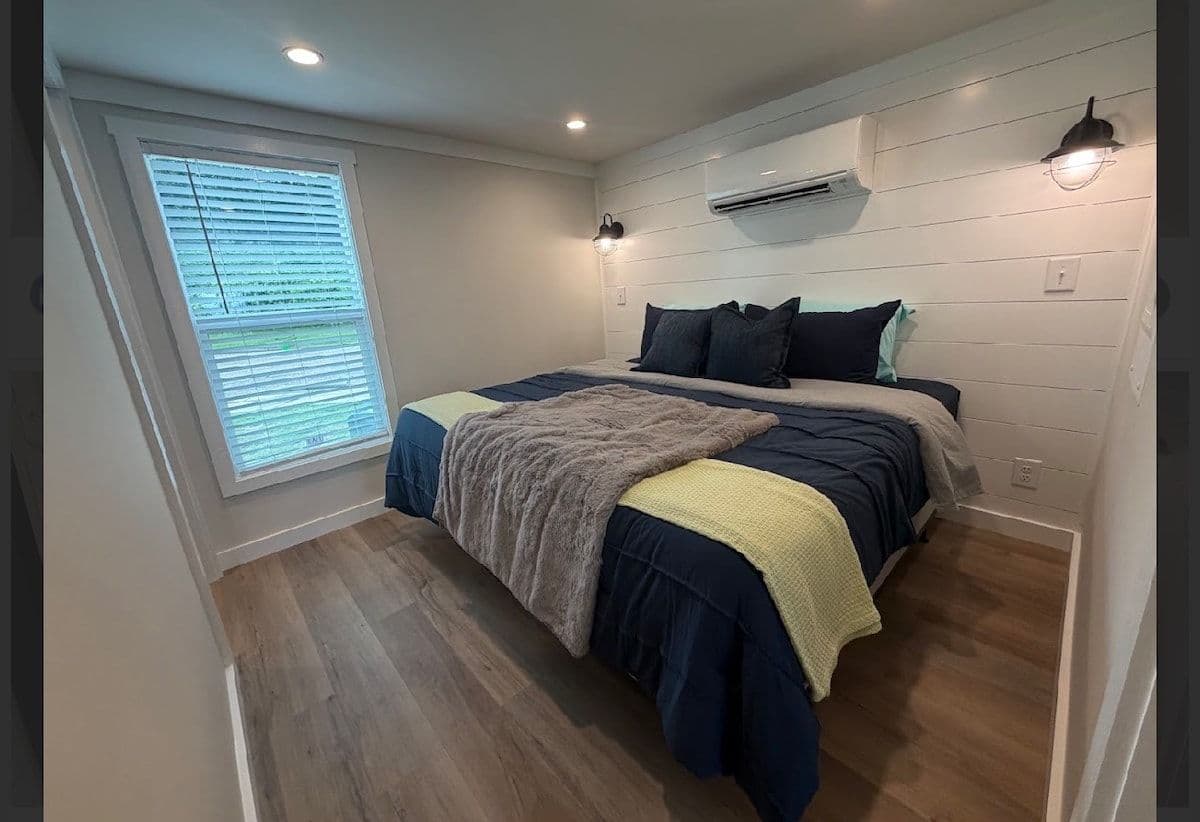 Bedroom with navy, yellow and gray bedding, window and wall AC