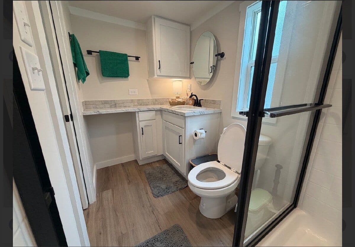 Bathroom vanity with green towels, round mirror, toilet and glass shower