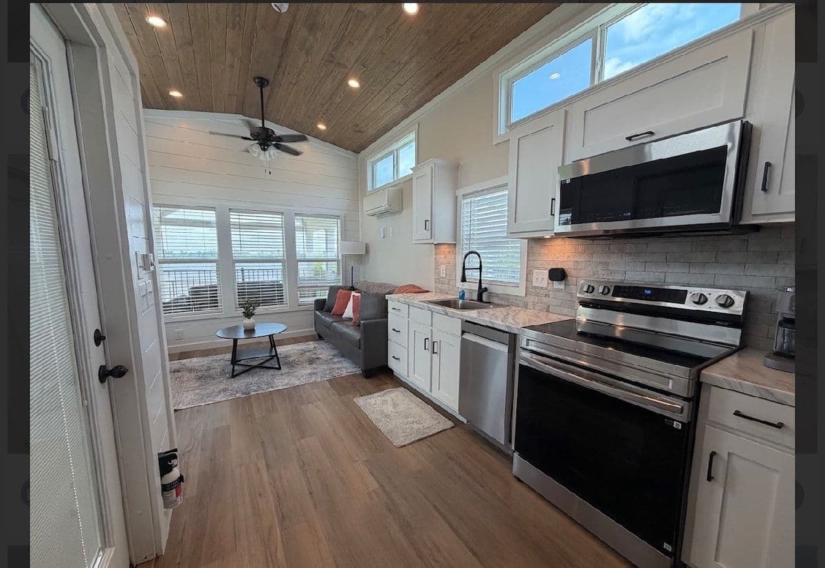 Galley kitchen with stainless range and microwave hood, white cabinets, marble counter, wood floor
