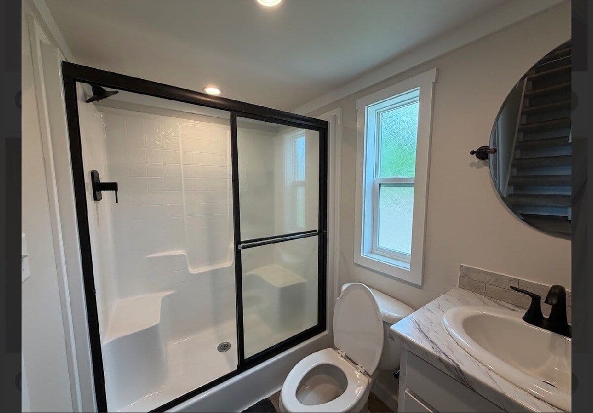 Bathroom with walk-in glass-door shower, round mirror and window to the river