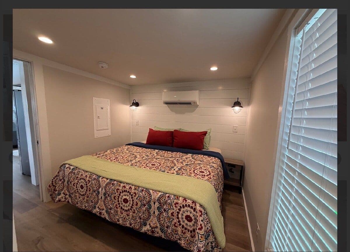 Main-floor bedroom, queen bed with coral patterned spread, wall AC, window shutters
