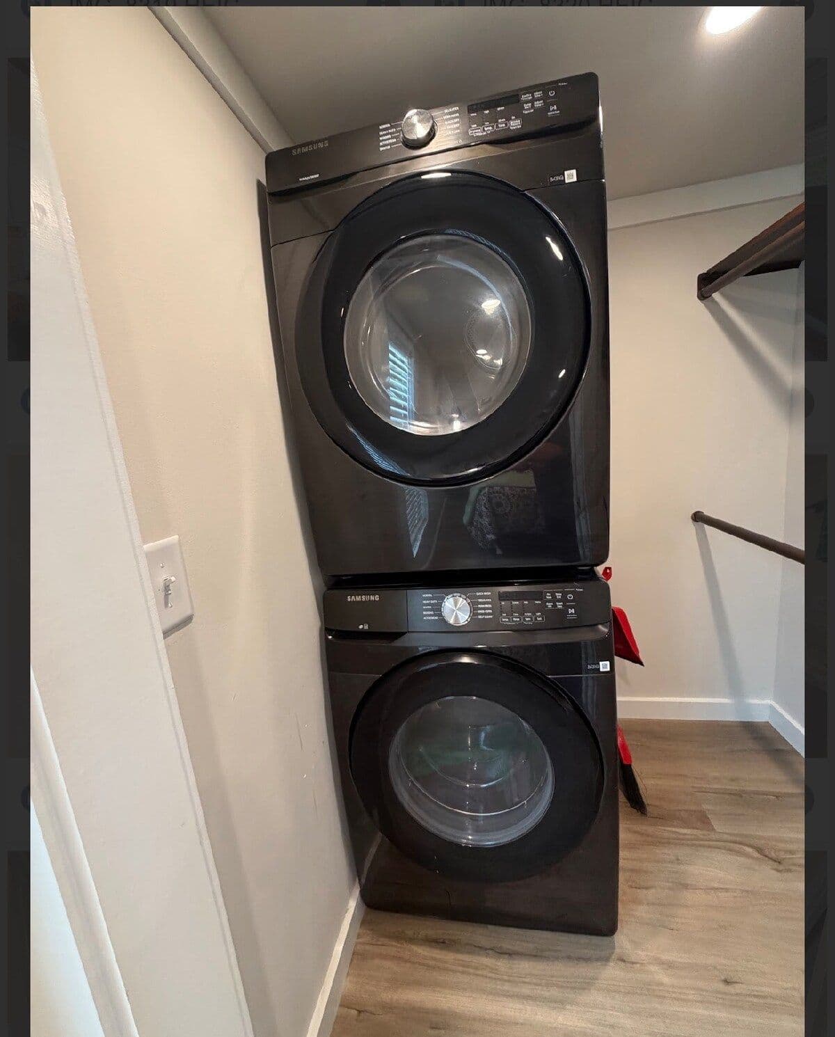 Laundry closet with stacked black washer and dryer and hanging rod (small appliance logo on control panel)