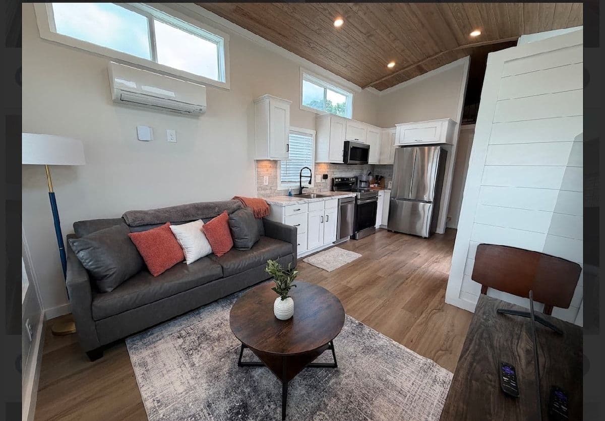 Living area with gray sofa, coral pillows, TV and rug under a wood-plank vaulted ceiling