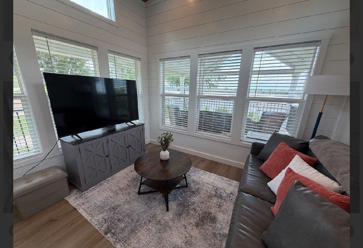 Living area from the window side: TV console, sofa with coral pillows, round coffee table
