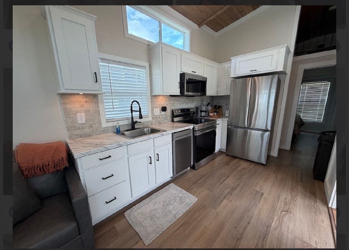 Kitchen from the living side: white cabinets, stainless fridge, window over the sink