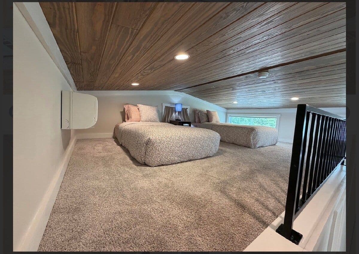 Loft from the stair rail: carpeted open floor and a bed under the wood ceiling