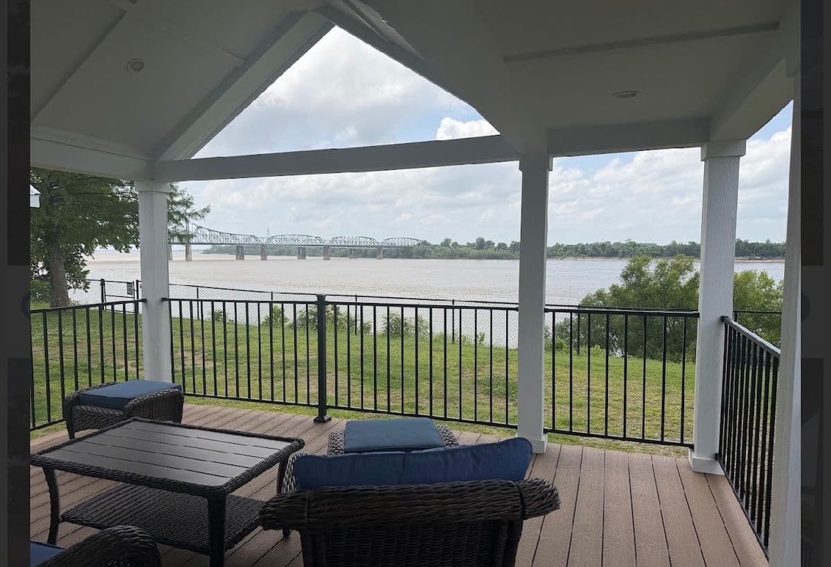 Screened covered porch with blue cushioned seating and a river and bridge view