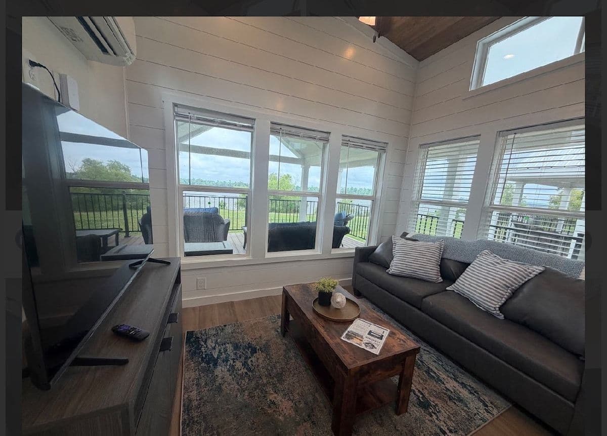 Living area with gray sofa, TV and wood coffee table by a wall of windows