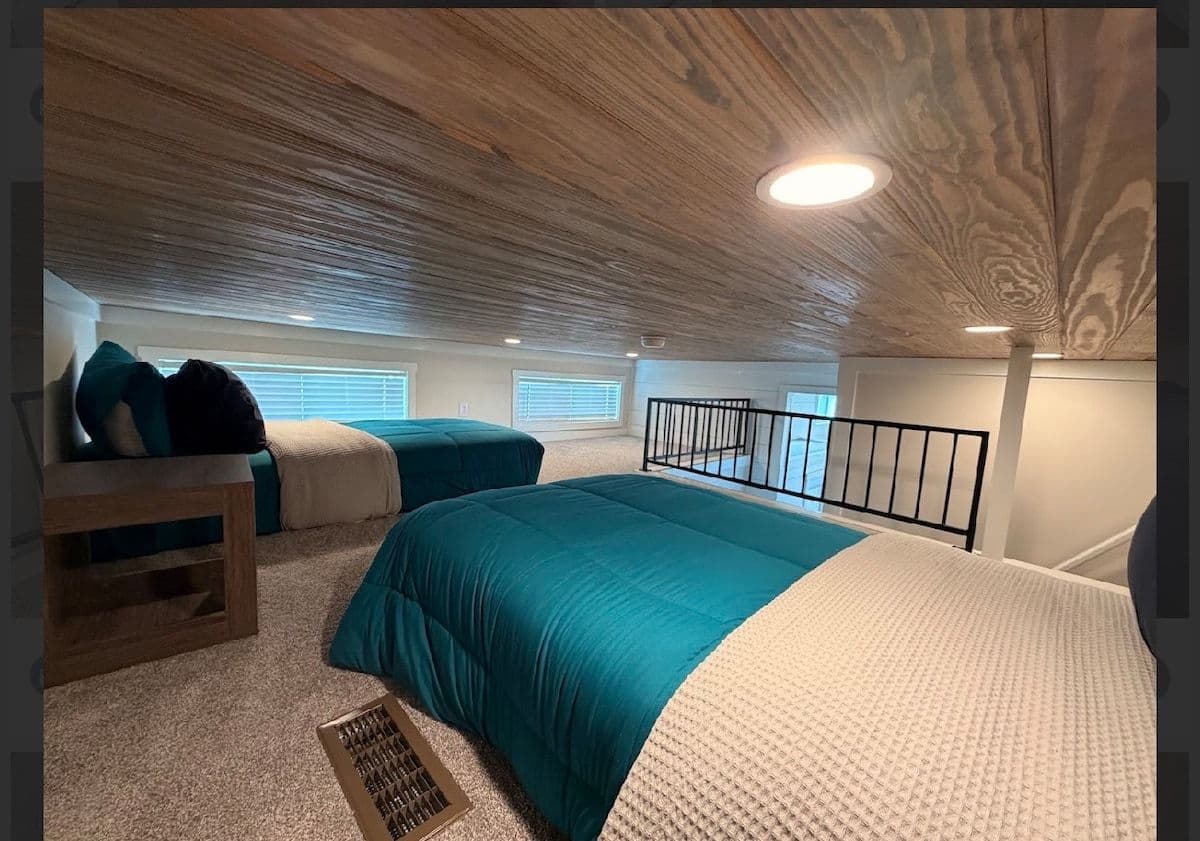 Loft with teal bedding, plank ceiling and stair rail