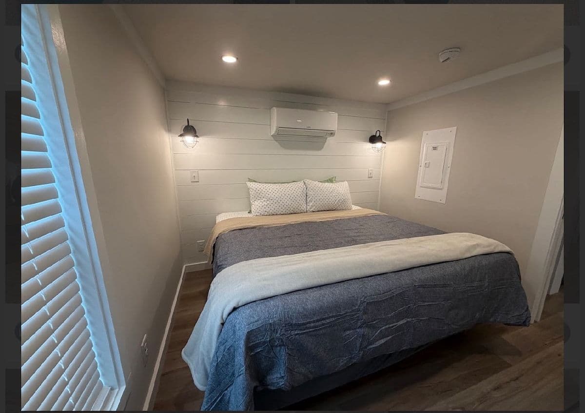 Bedroom with blue and tan bedding, wall AC, recessed lights