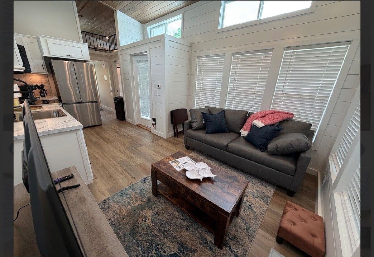 Living area with gray sofa, red pillow and wood coffee table, kitchen behind