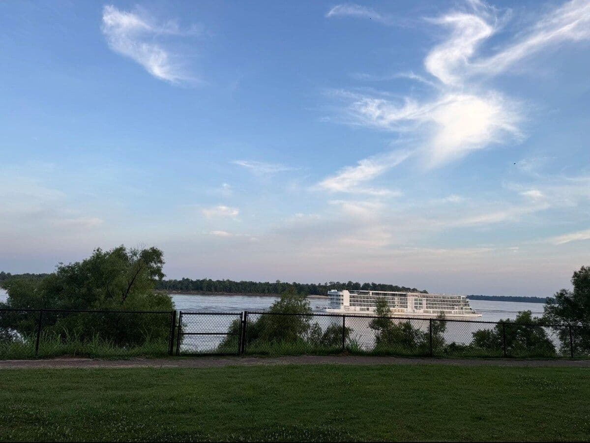 Lawn and river under a blue sky with a boat in the distance