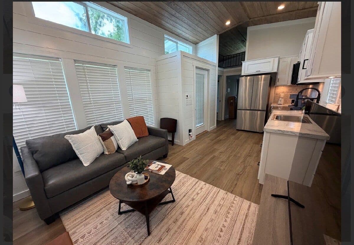 Living area with gray sofa, oval coffee table and rug, kitchen behind