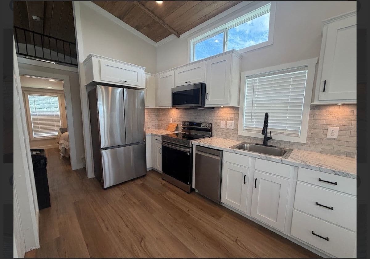Kitchen with stainless fridge and range, white cabinets, stair rail above