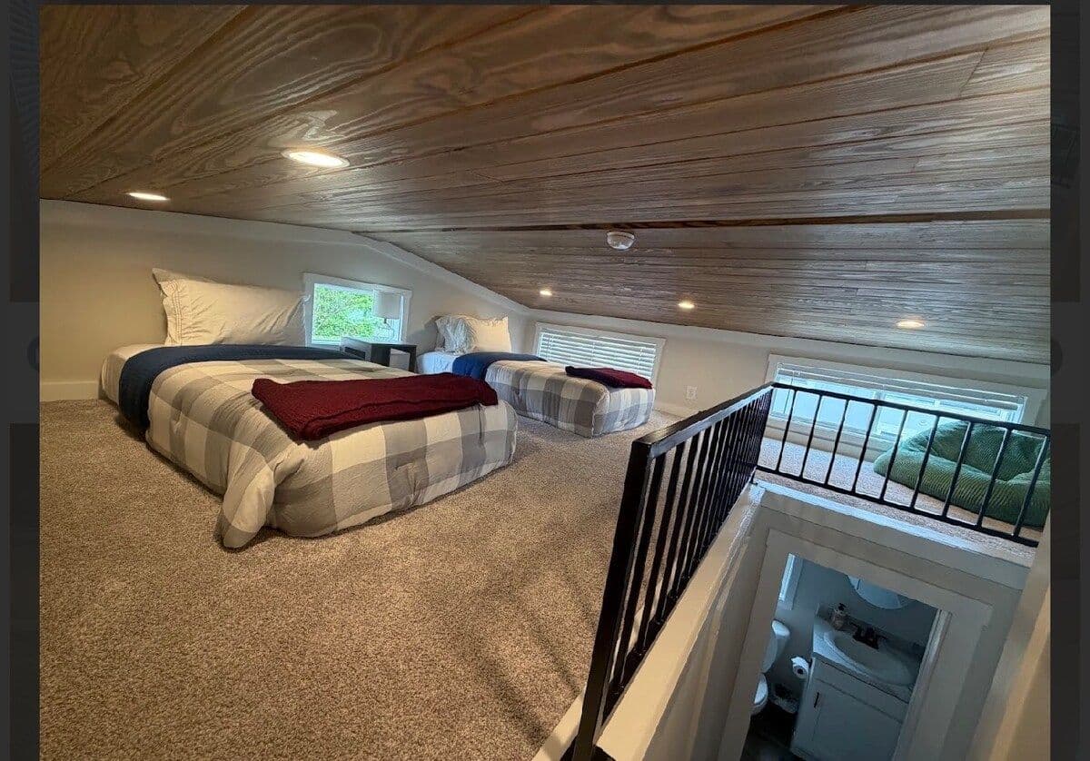 Loft with plaid bed and red blanket, stair opening, plank ceiling