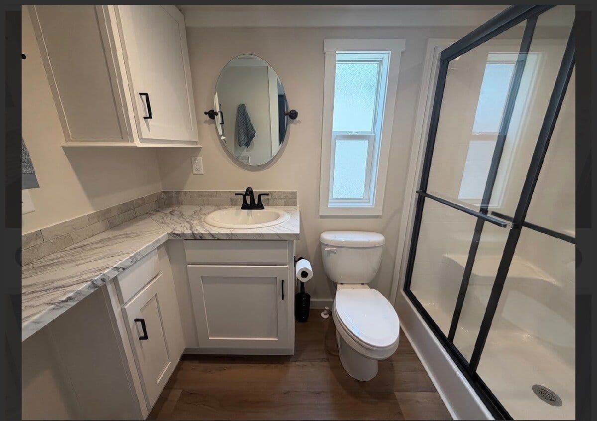 Bathroom with white vanity, round mirror, toilet and glass shower