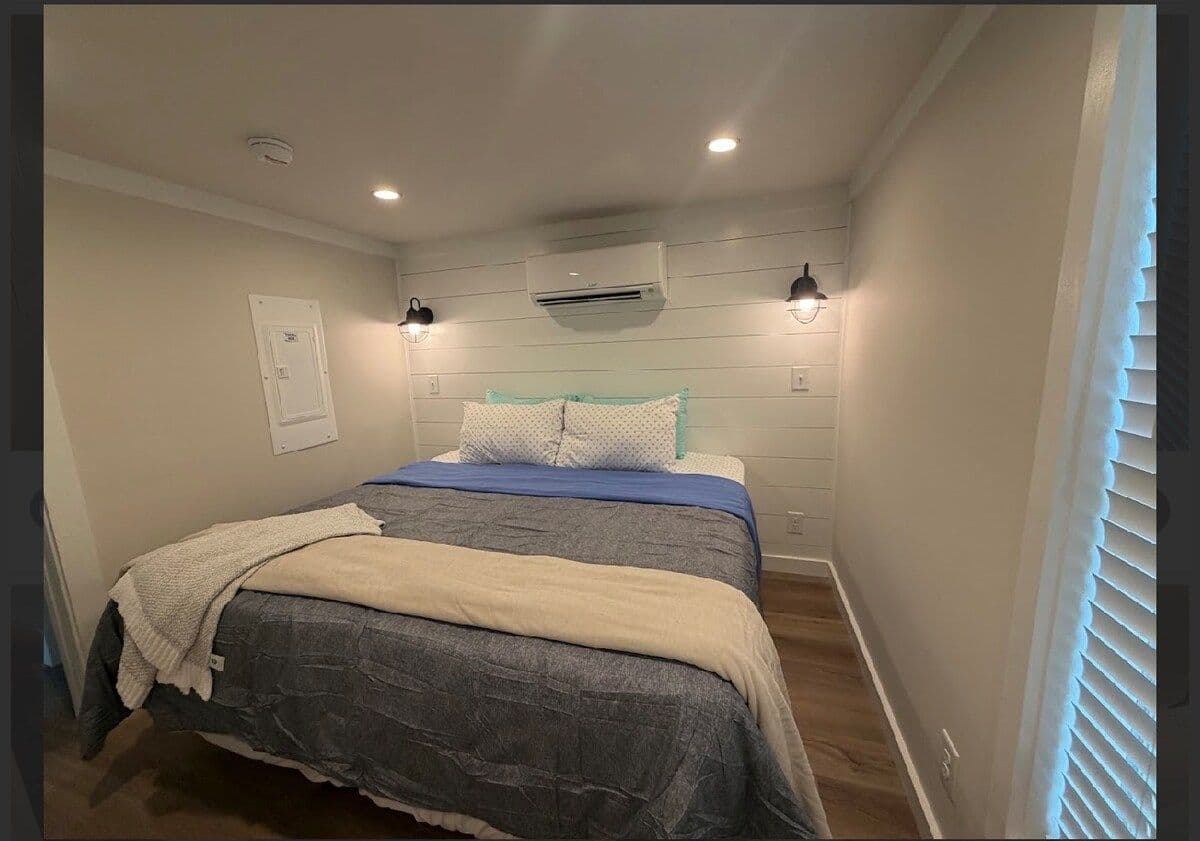 Bedroom with gray and white bedding, wall AC, sconce lights