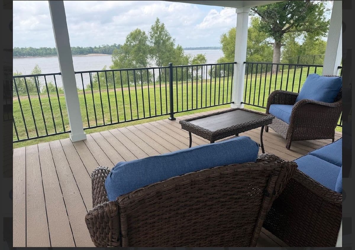 Covered porch with blue wicker seating overlooking the lawn and river