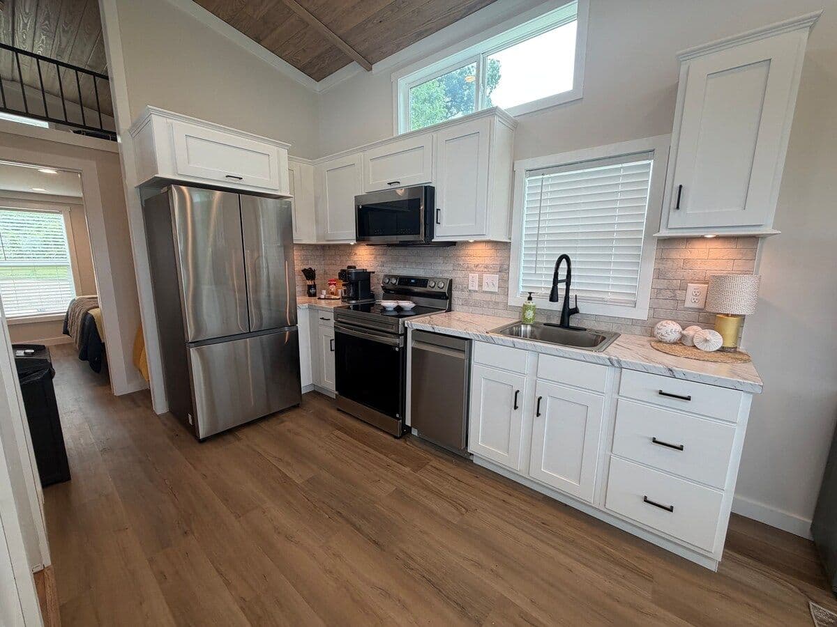Kitchen with stainless fridge and range, white cabinets, sink under a window