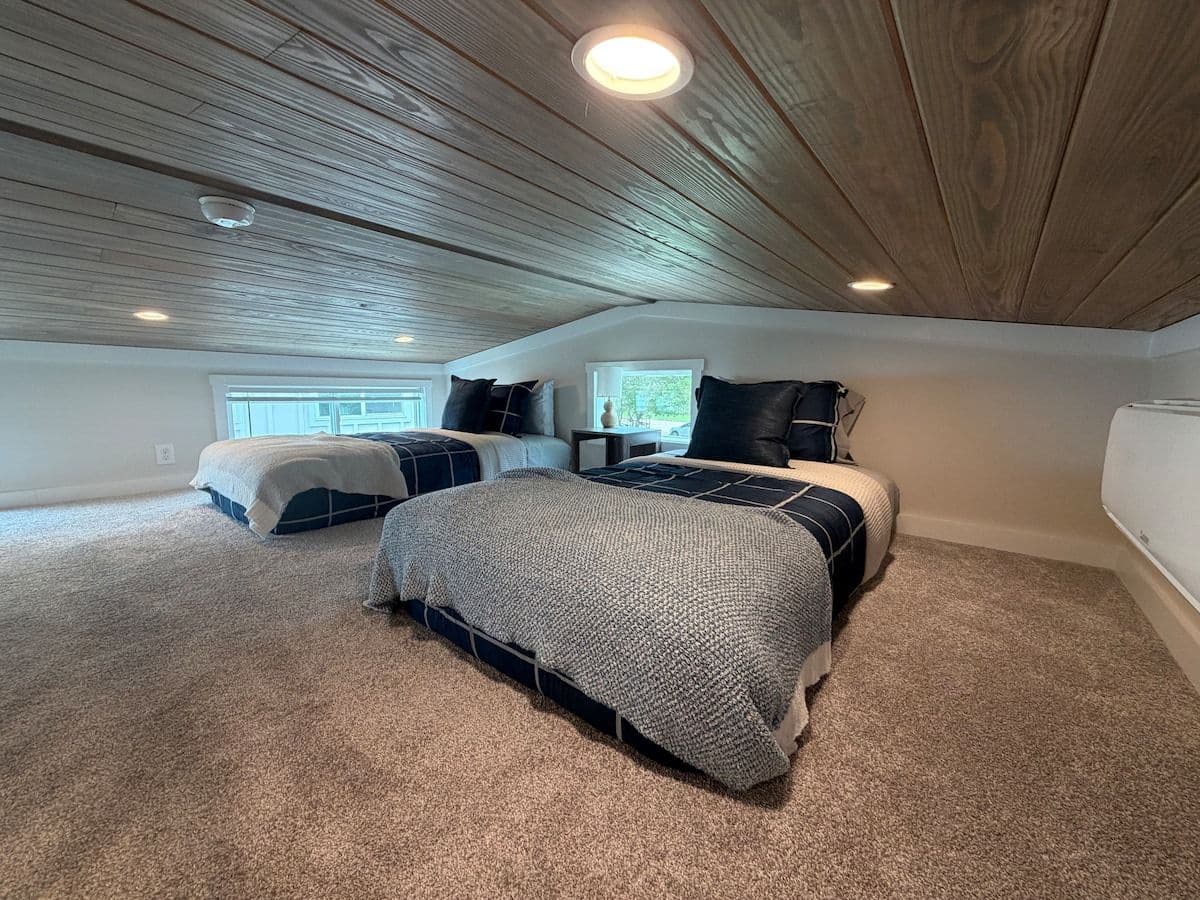 Loft with two beds in gray bedding under a wood-plank ceiling