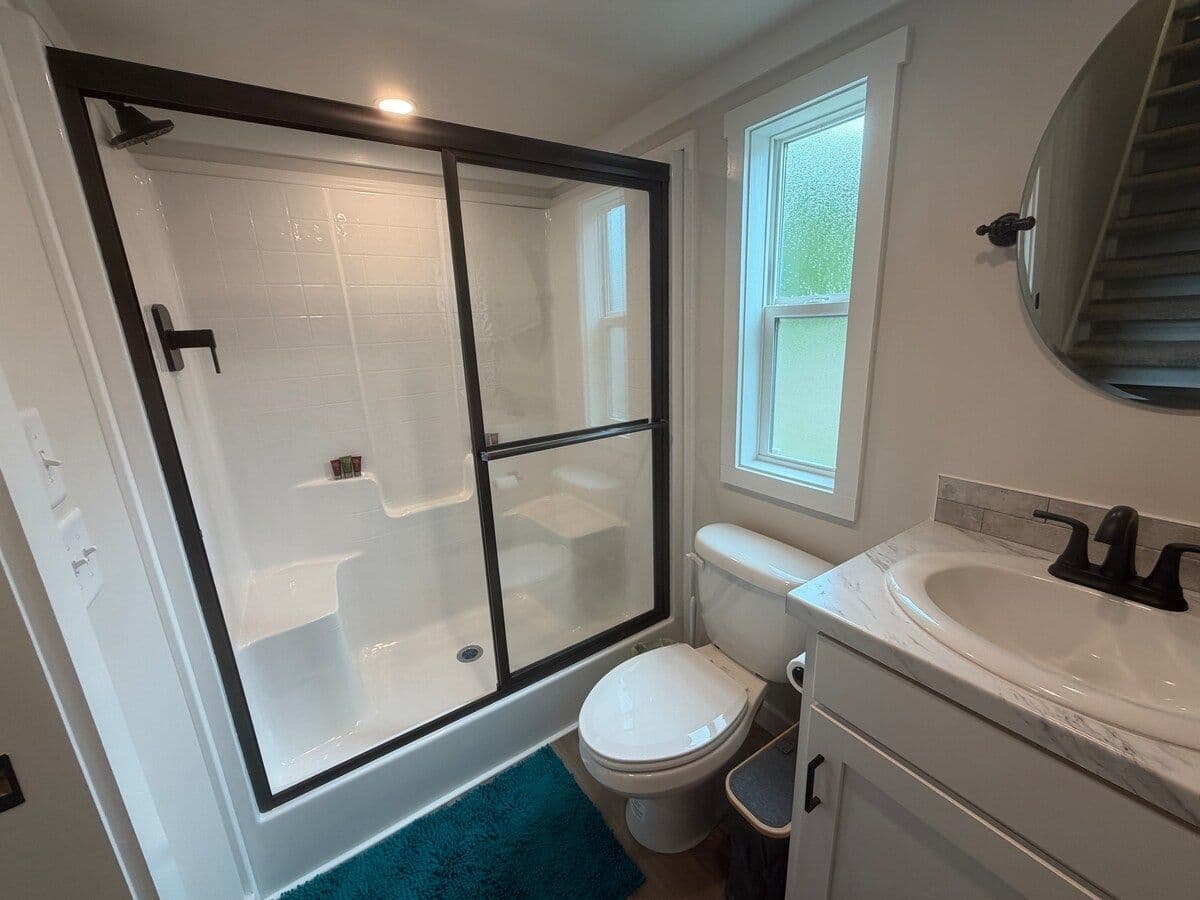 Bathroom with glass walk-in shower, round mirror, white vanity and teal rug