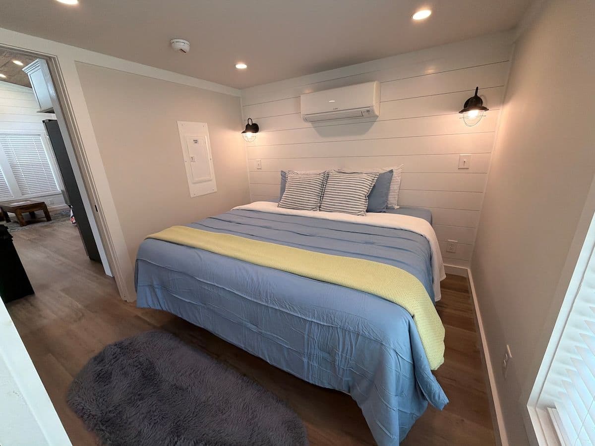 Bedroom with blue and yellow-striped bedspread and gray rug, wall AC