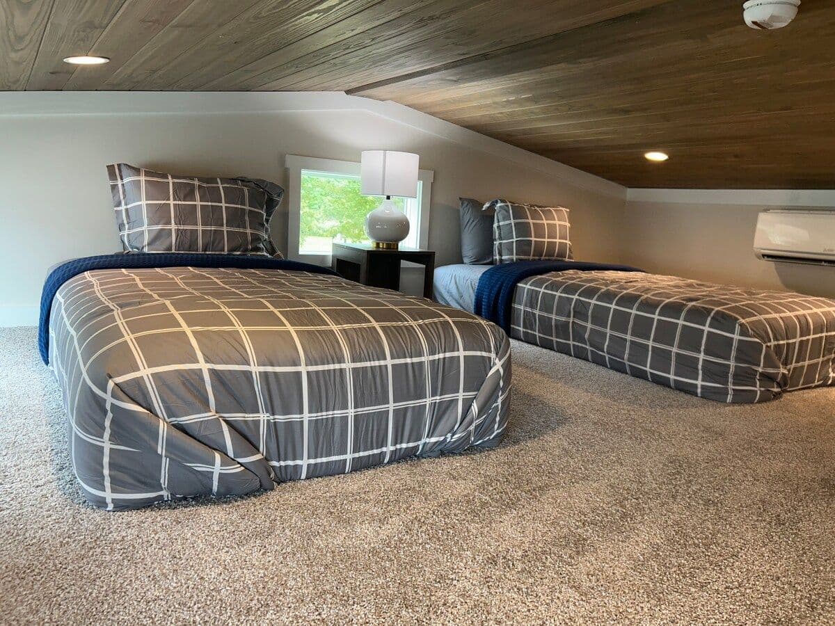 Loft with plaid-spread beds, carpet and wood plank ceiling