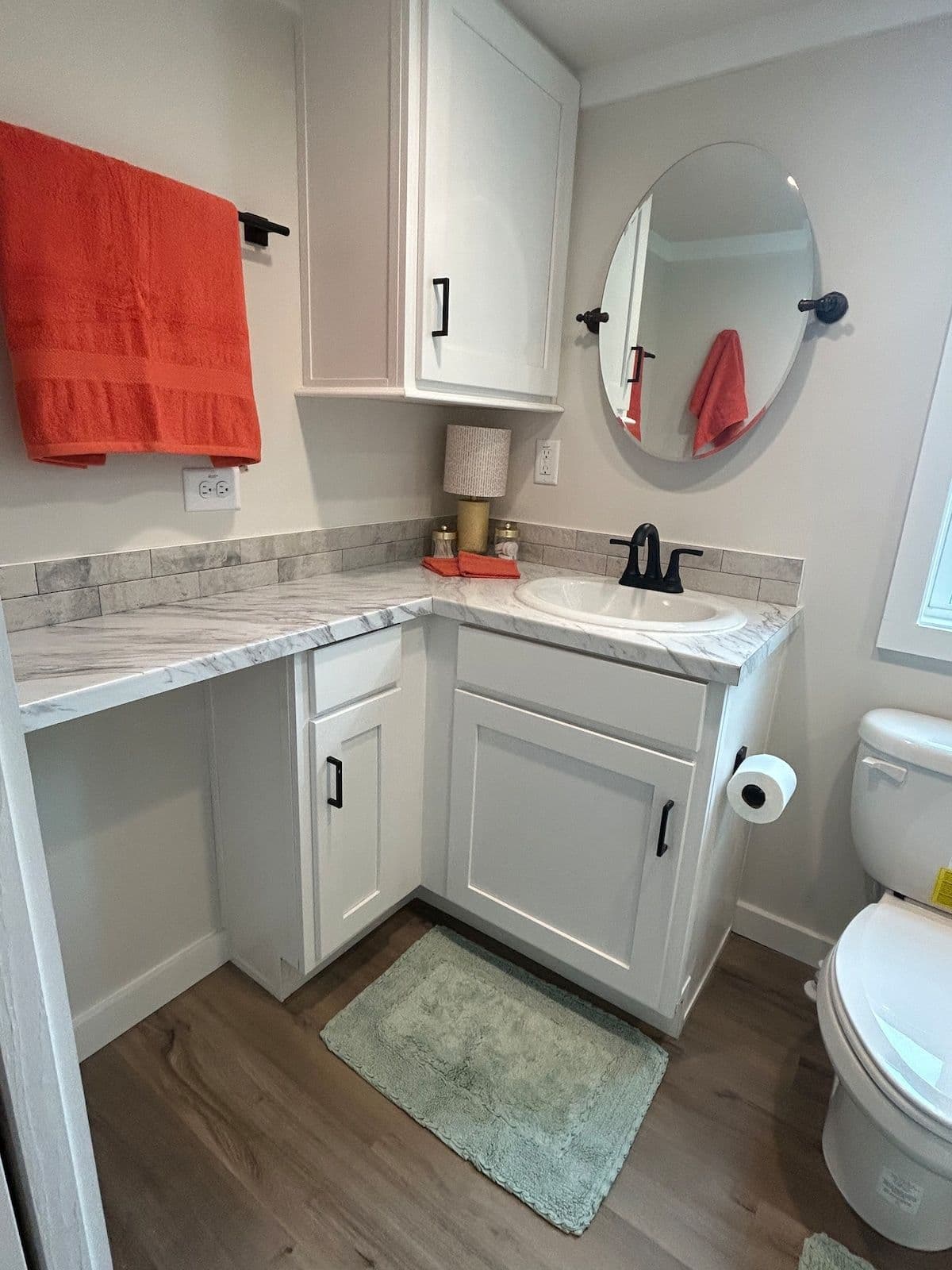 Bathroom with orange towel, round mirror, vanity and toilet