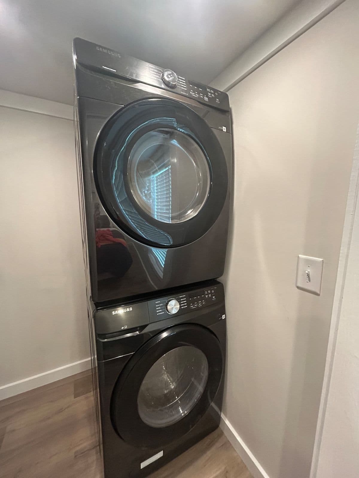 Laundry closet with stacked black washer and dryer (small appliance logo on control panel)