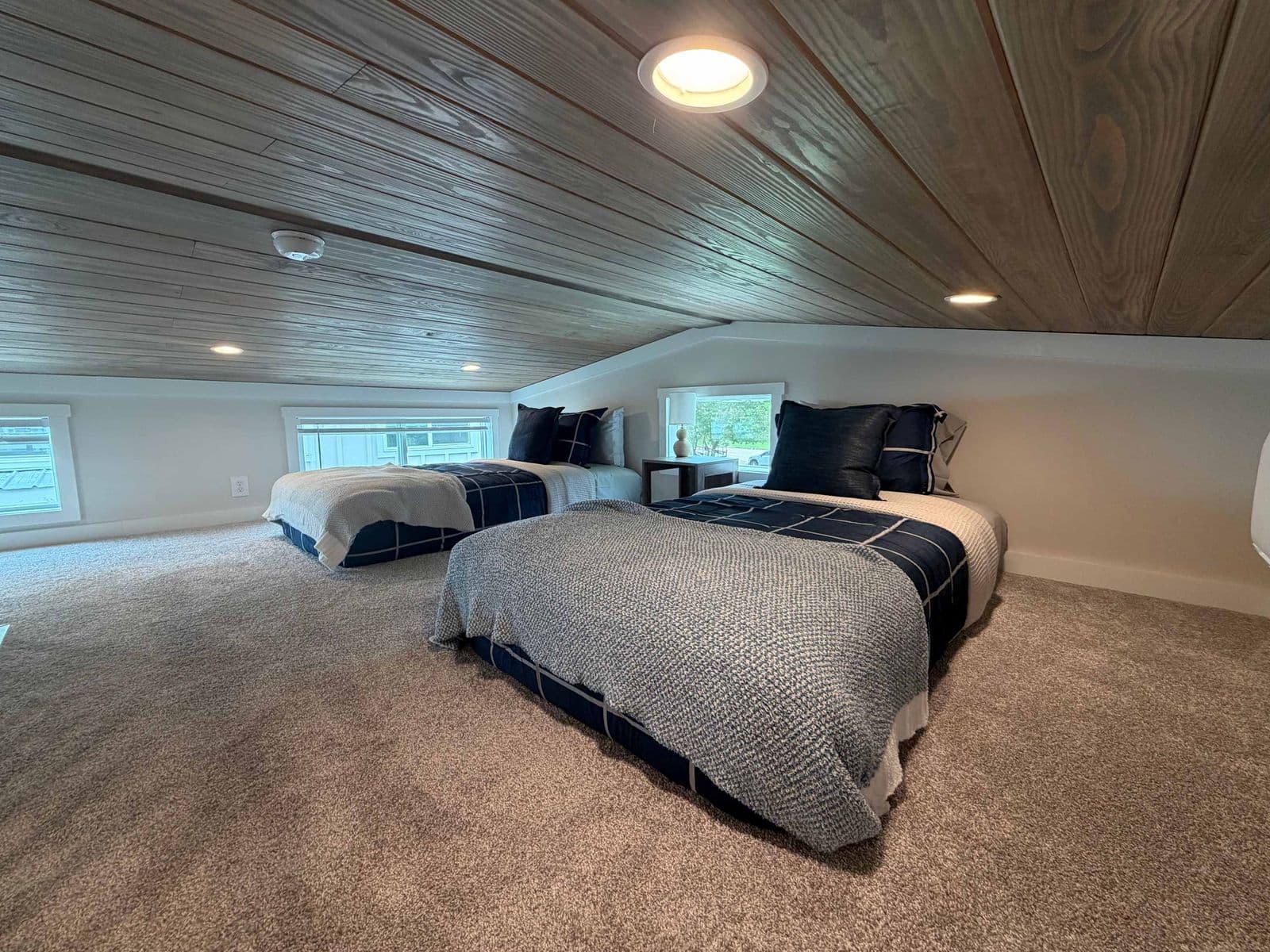 Loft with two beds, gray bedding and a plank ceiling