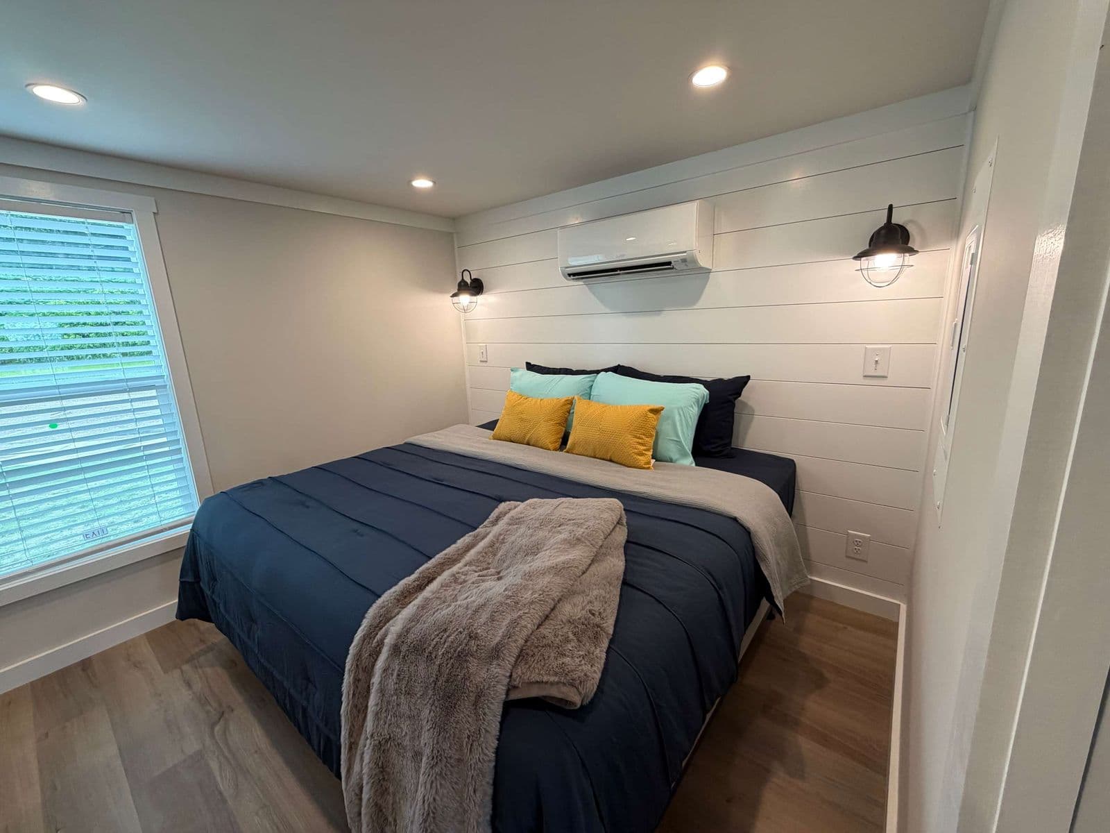 Bedroom with navy bedding, yellow pillows and a gray throw, wall AC