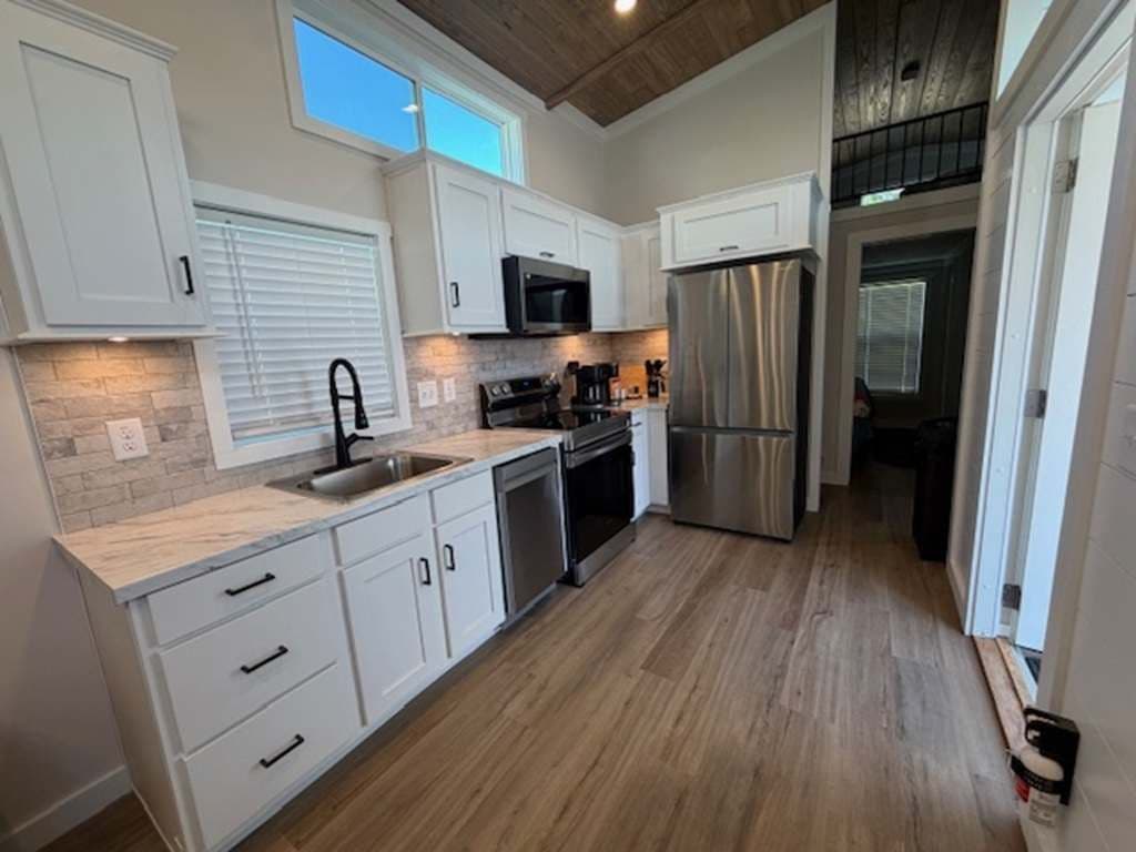 Kitchen with stainless fridge, white cabinets, black faucet and wood floor