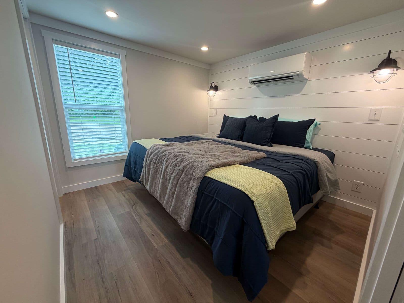 Bedroom with navy and yellow bedding, window with shutters, wall AC