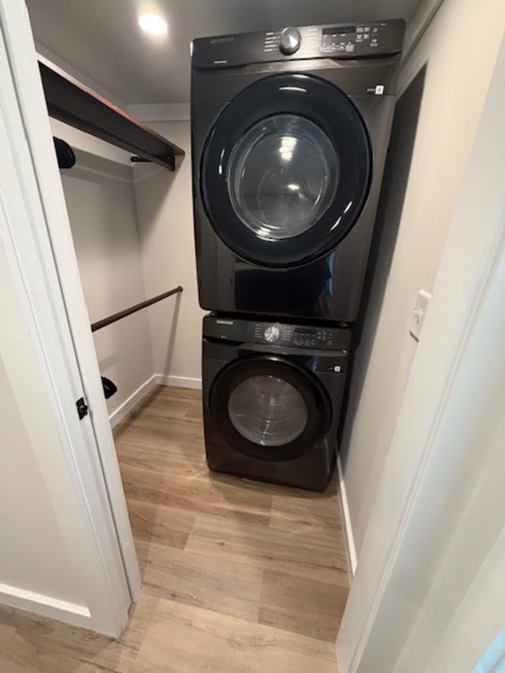 Laundry closet with stacked black washer and dryer and hanging rod (small appliance logo on control panel)