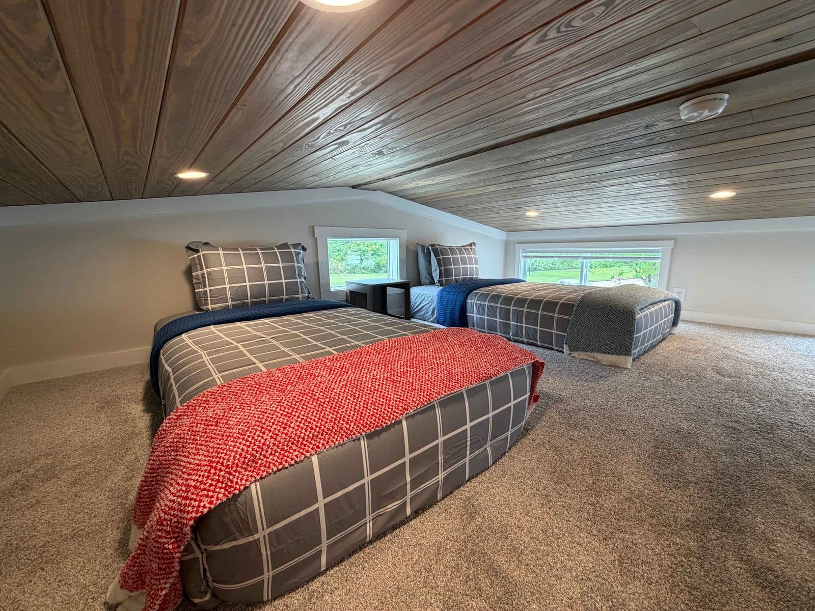 Loft with red-and-plaid bed under a wood ceiling