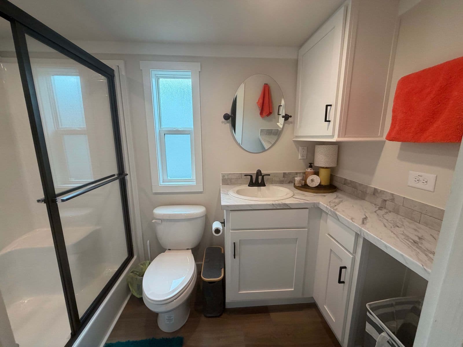 Bathroom with glass shower, round mirror, red towel and toilet