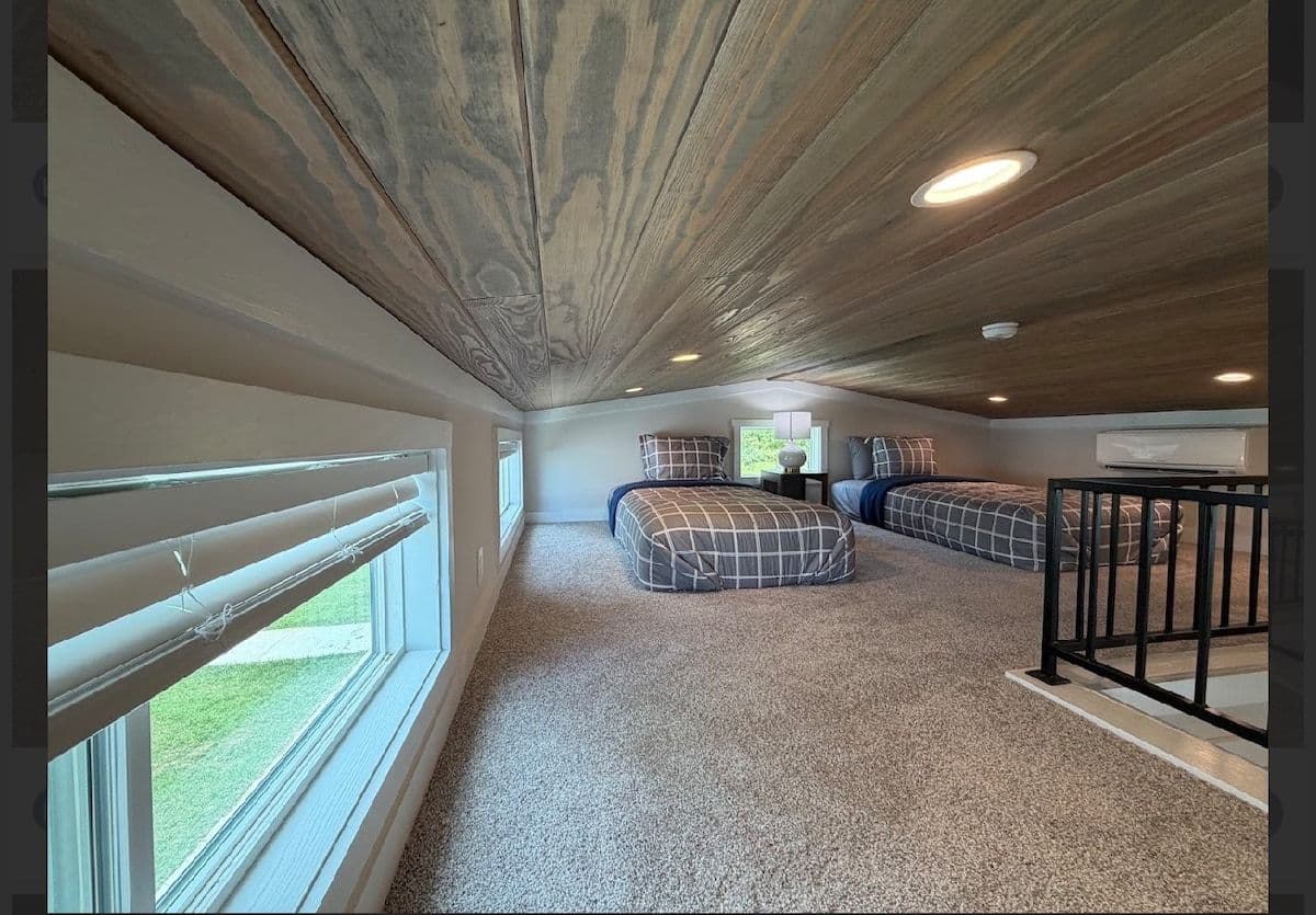 Loft from the stair rail: carpet, window and two beds under a wood ceiling