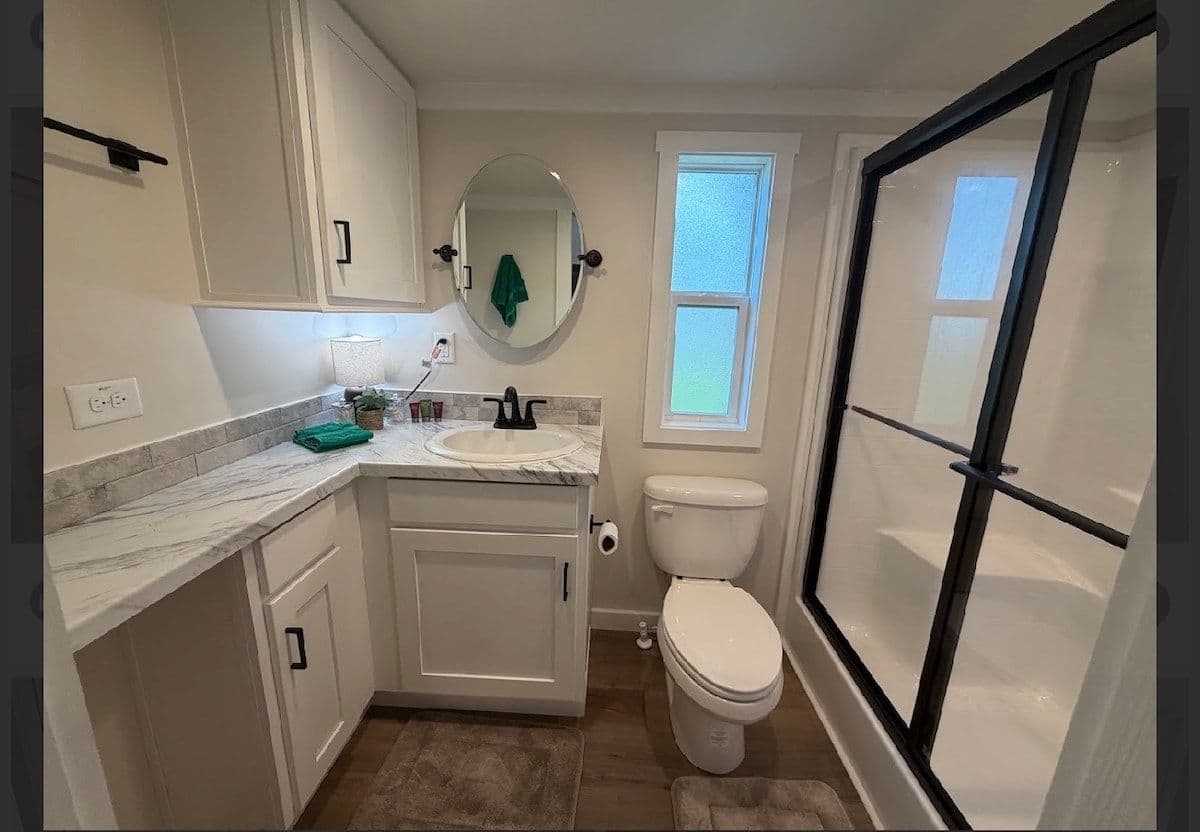 Bathroom with black-framed glass shower, white vanity and toilet
