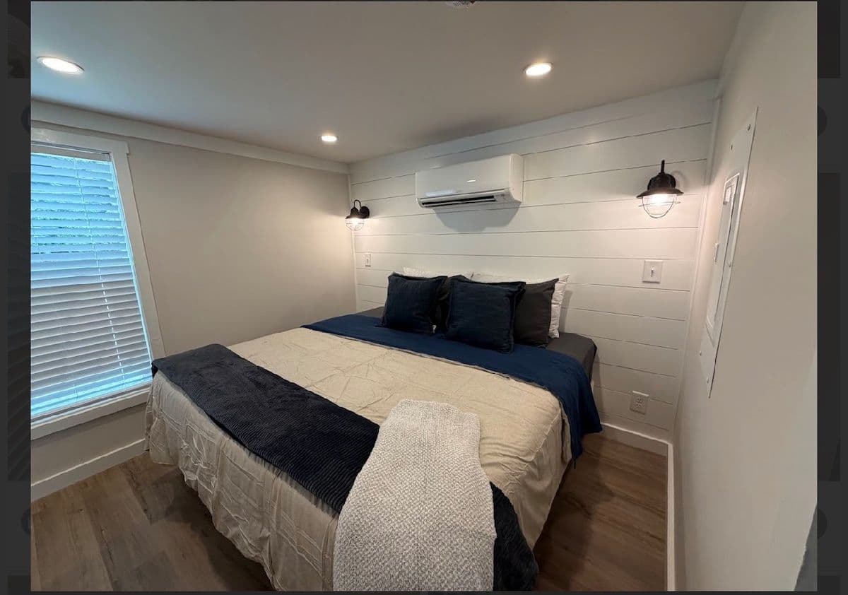 Bedroom with white and navy bedding, wall AC and shuttered window