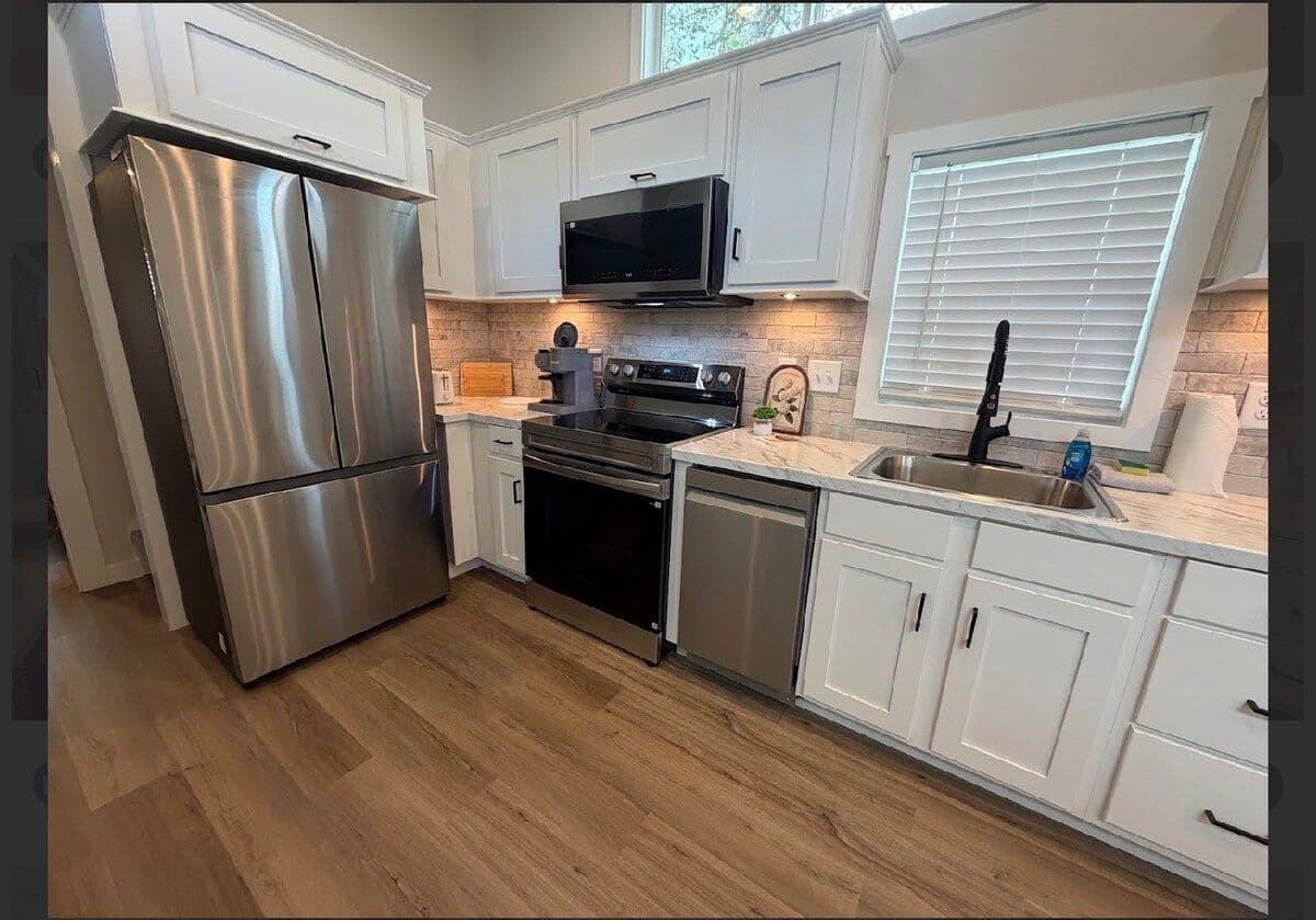 Kitchen with stainless fridge and range, white cabinets, window
